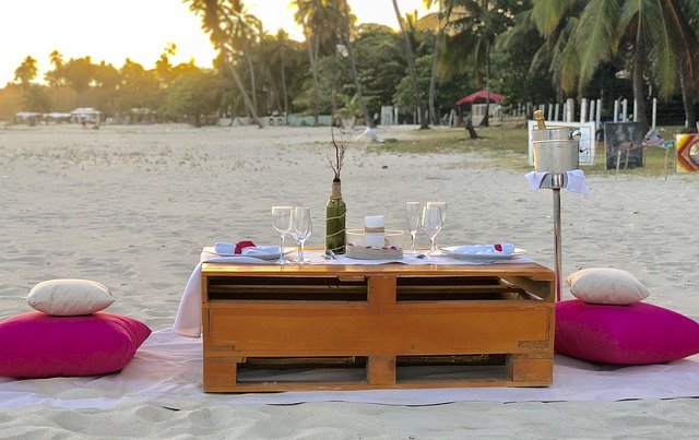 Stolik na plaży z winem oraz kieliszkami przygotowany na romantyczną kolację dla dwojga